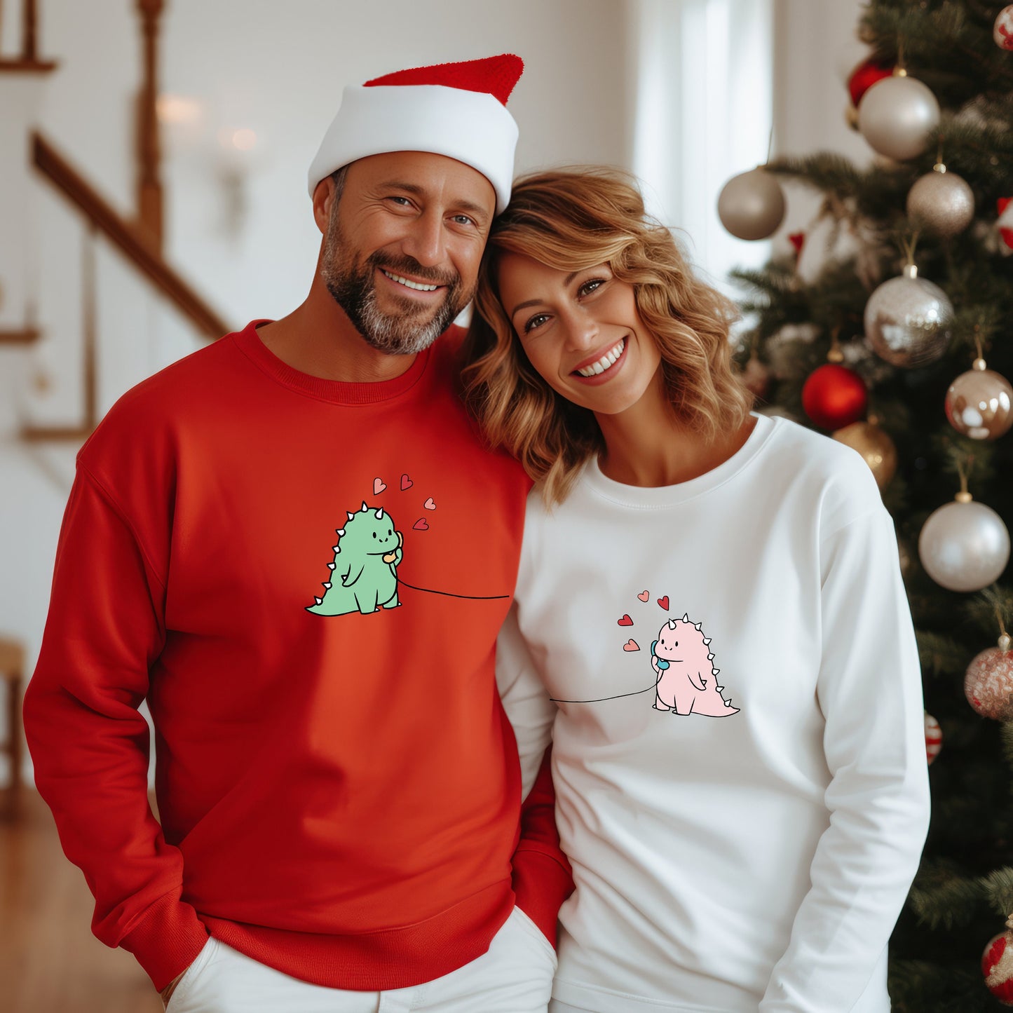 A man in red and a woman in white wearing matching sweatshirts with cartoon dinosaurs and hearts, posing indoors.