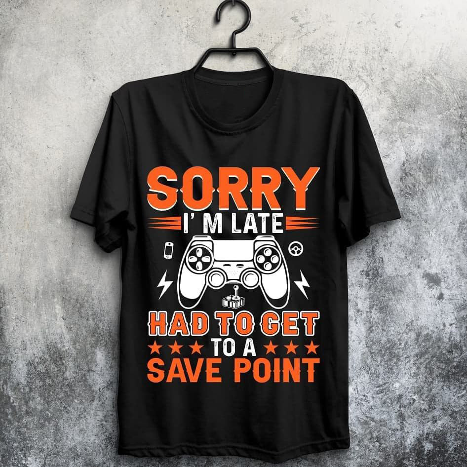 Black t-shirt with orange and white text "SORRY I'M LATE HAD TO GET TO A SAVE POINT" and a game controller graphic.