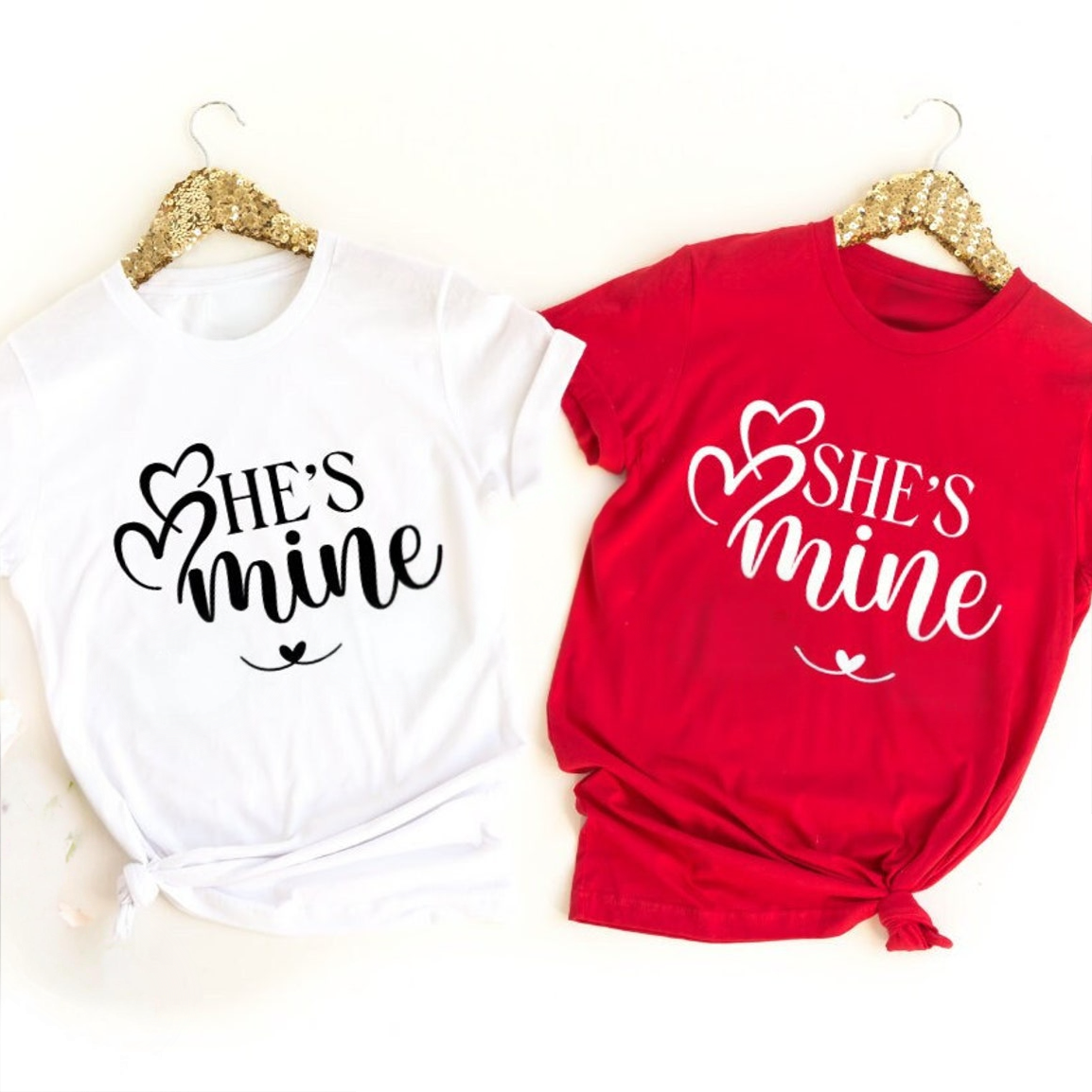 A white t-shirt reading "He's Mine" with a heart and a red t-shirt reading "She's Mine" with a heart.