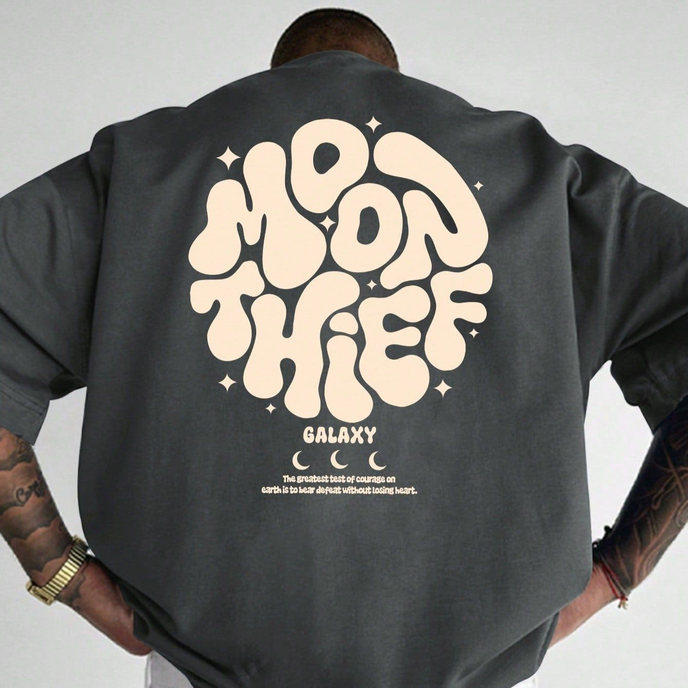 Dark-colored oversized t-shirt with a "Moon Thief" graphic in a rounded font, "Galaxy" text, star accents, and a short quote on the back.