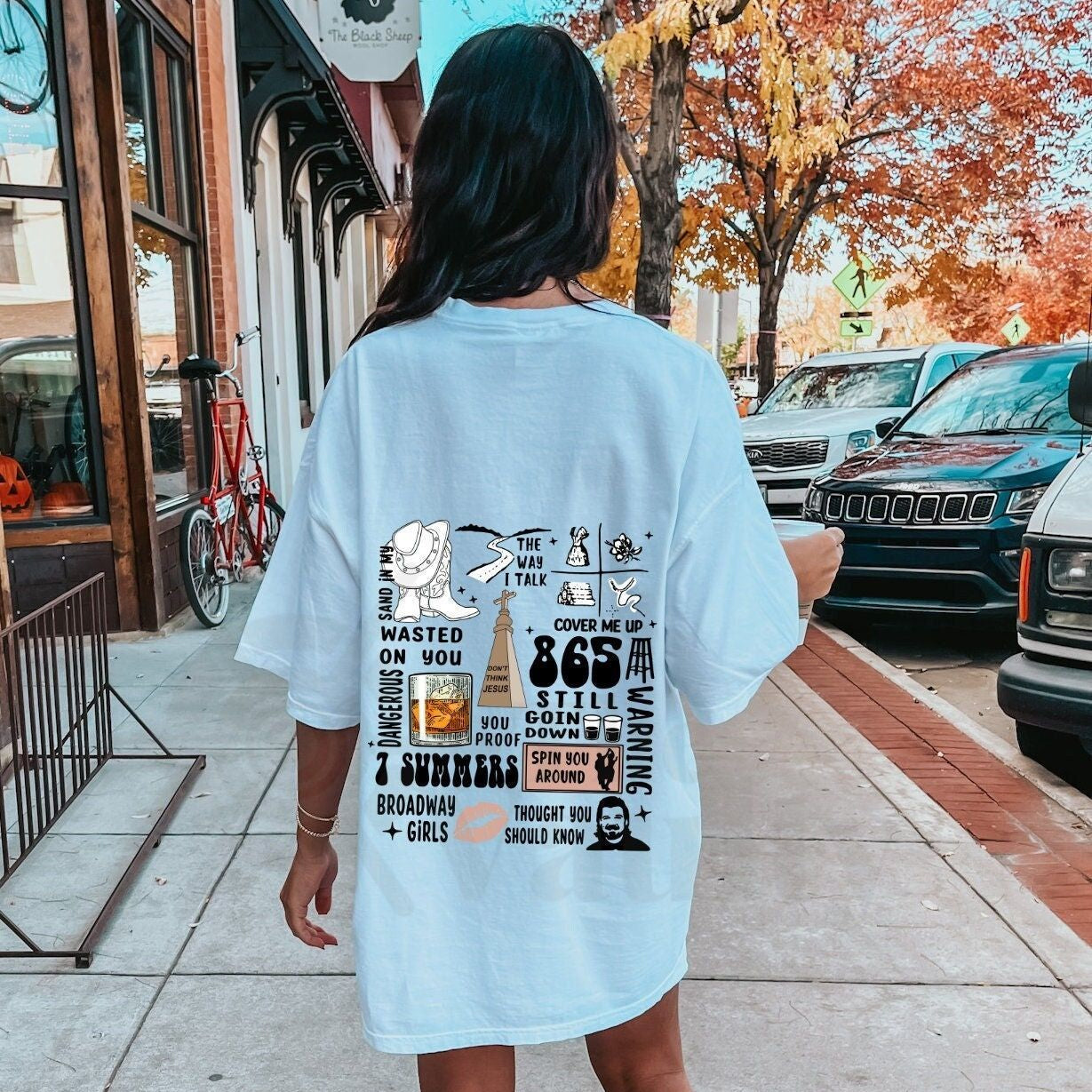 Light-colored oversized t-shirt with a collage of Morgan Wallen song titles and related graphics printed on the back.