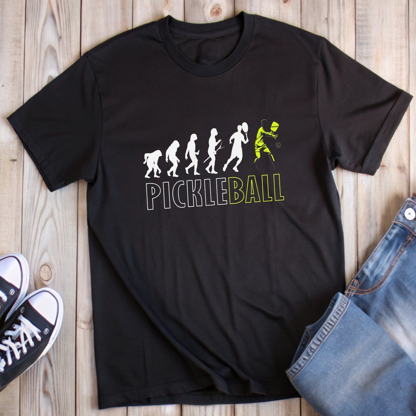 Black t-shirt with "Pickleball" text and evolution graphic ending in a pickleball player.
