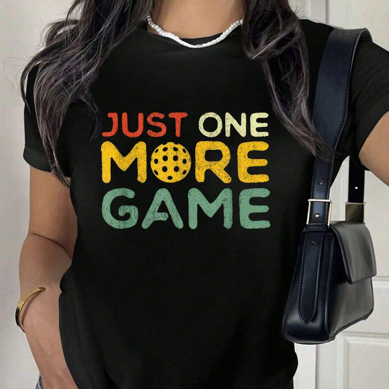 Black t-shirt with "Just one more game" text and pickleball graphic in retro colors.
