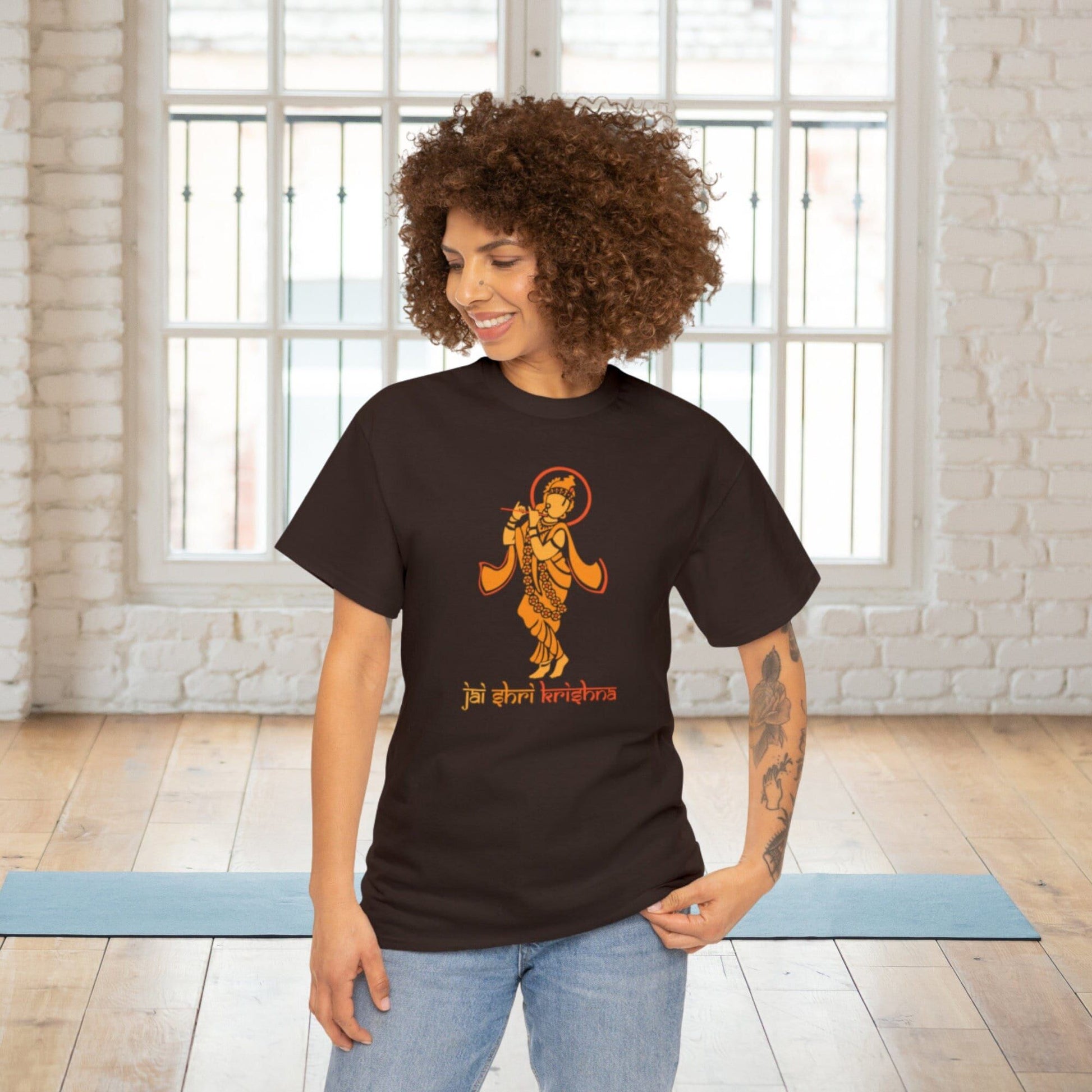 Dark brown t-shirt with an orange ethnic-style illustration of Krishna playing the flute and "Jai Shri Krishna" written in Morden Devanagari script below.