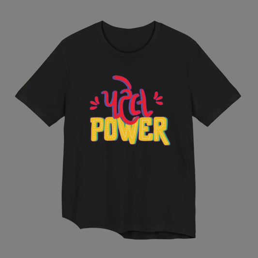 Black t-shirt with the Gujarati word "પટેલ" (Patel) in a colorful, stylized font above the English word "POWER" in a similar font. The t-shirt is displayed with a background featuring illustrated Gujarati snacks and decorative patterns. Cotton blend t-shirts, available in various sizes.