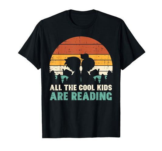 Black t-shirt with "All the Cool Kids Are Reading" and a retro sunset graphic with silhouettes of two children reading.  A stylish design for book enthusiasts.