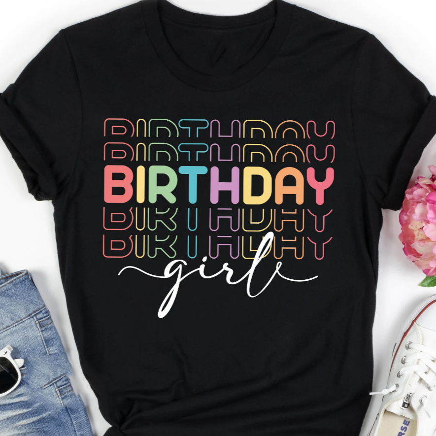 Black t-shirt with "Birthday" repeated in a retro rainbow font and "girl" in script. Casual, comfortable fit.