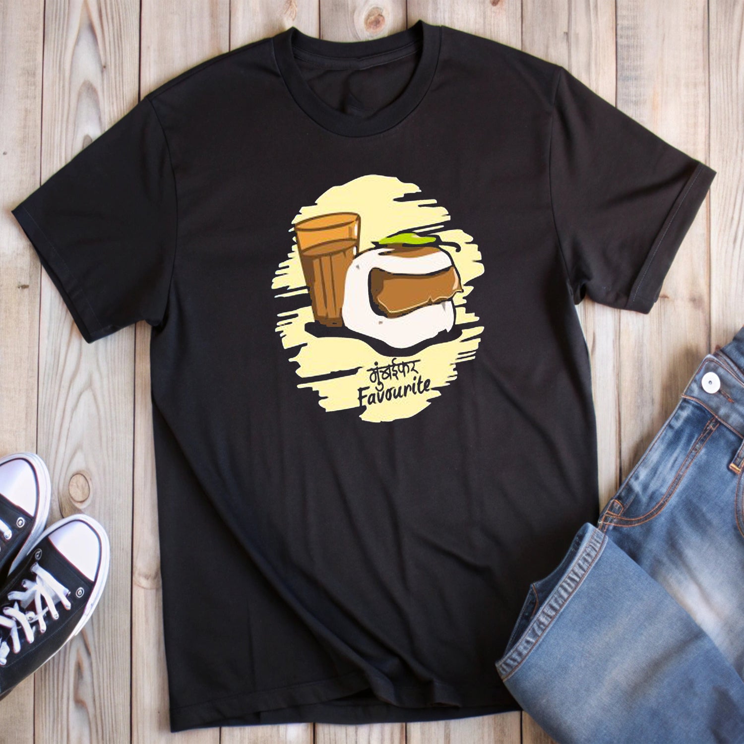 Black t-shirt with a graphic of vada pav, tea in a glass, and "मुंबईकर Favourite" text, styled with jeans and sneakers.