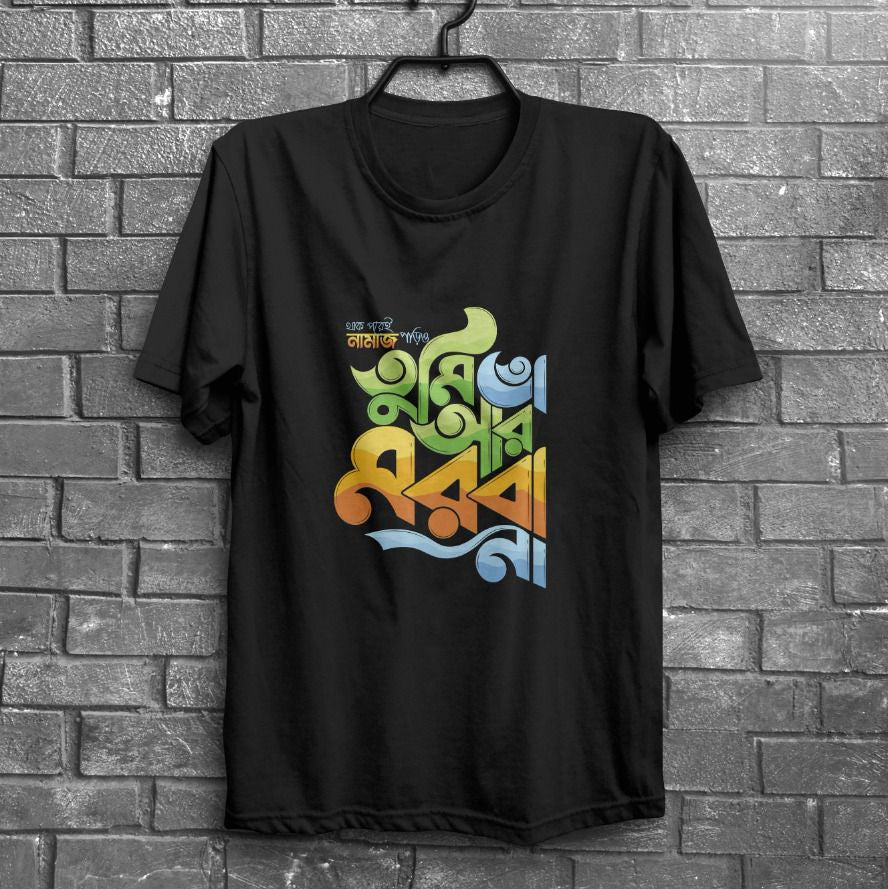 Black t-shirt with multicolored Bangla text hanging on a dark brick wall.