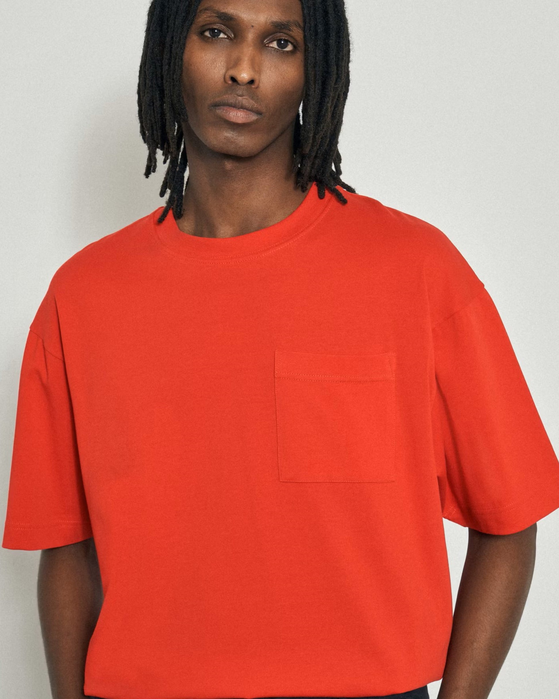  A close-up of a person with dark hair wearing a bright orange t-shirt with a pocket.