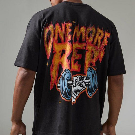 Black oversized t-shirt with a graphic on the back featuring the phrase "ONE MORE REP" in a fiery font above an illustration of a hand gripping a barbell. 