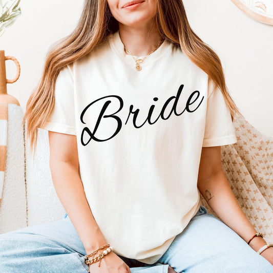 Cream-colored cotton t-shirt with the word "Bride" printed in a flowing black script font on the front.
