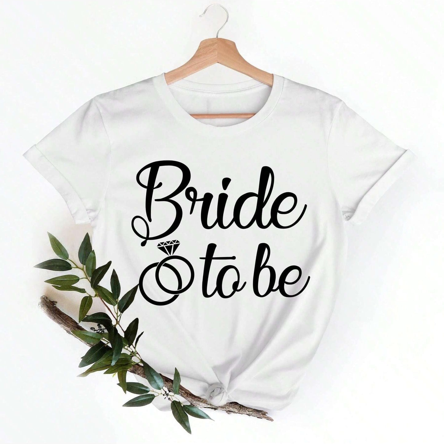White cotton t-shirt with "Bride" in cursive above a diamond ring graphic and "to be" in smaller cursive text.