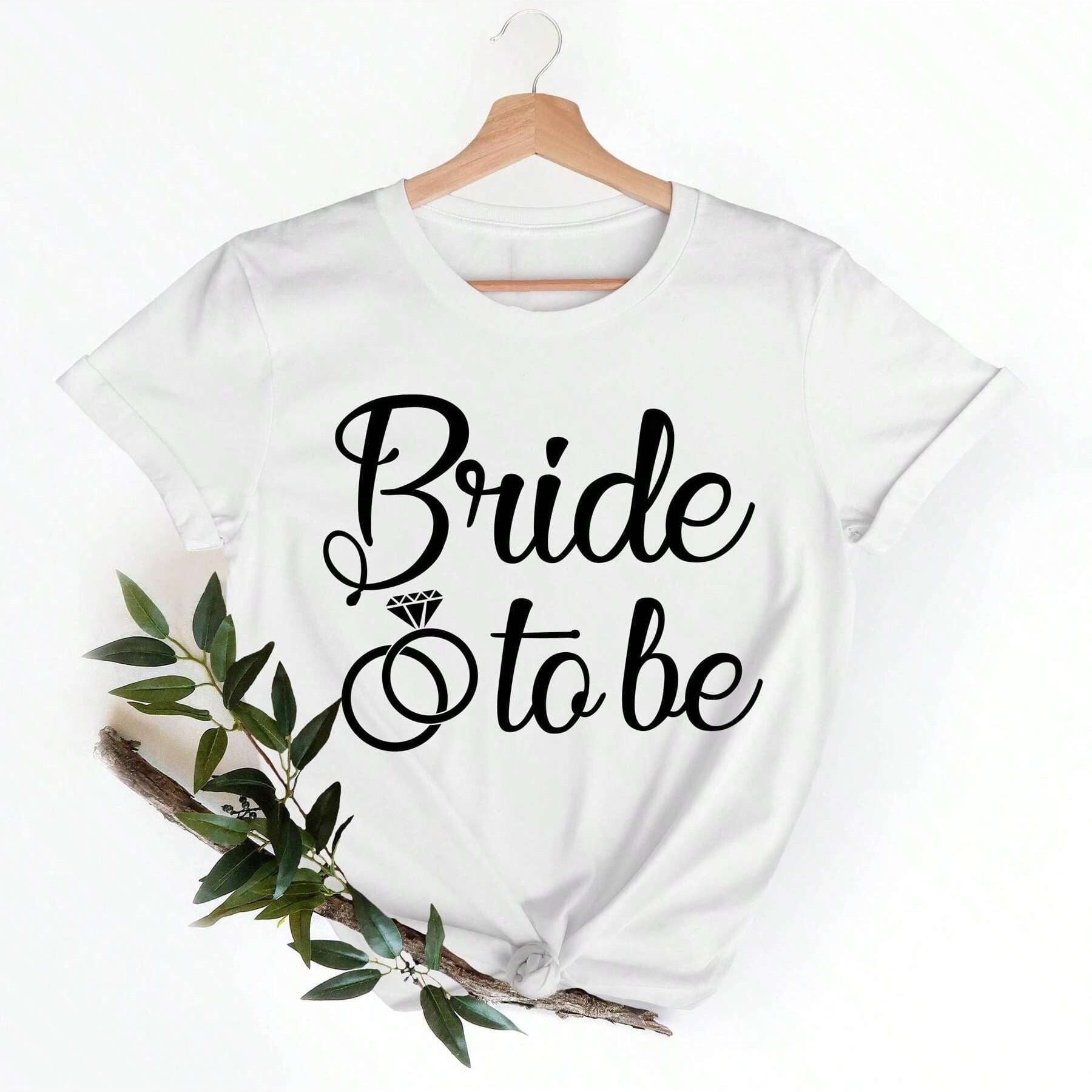 White cotton t-shirt with "Bride" in cursive above a diamond ring graphic and "to be" in smaller cursive text.