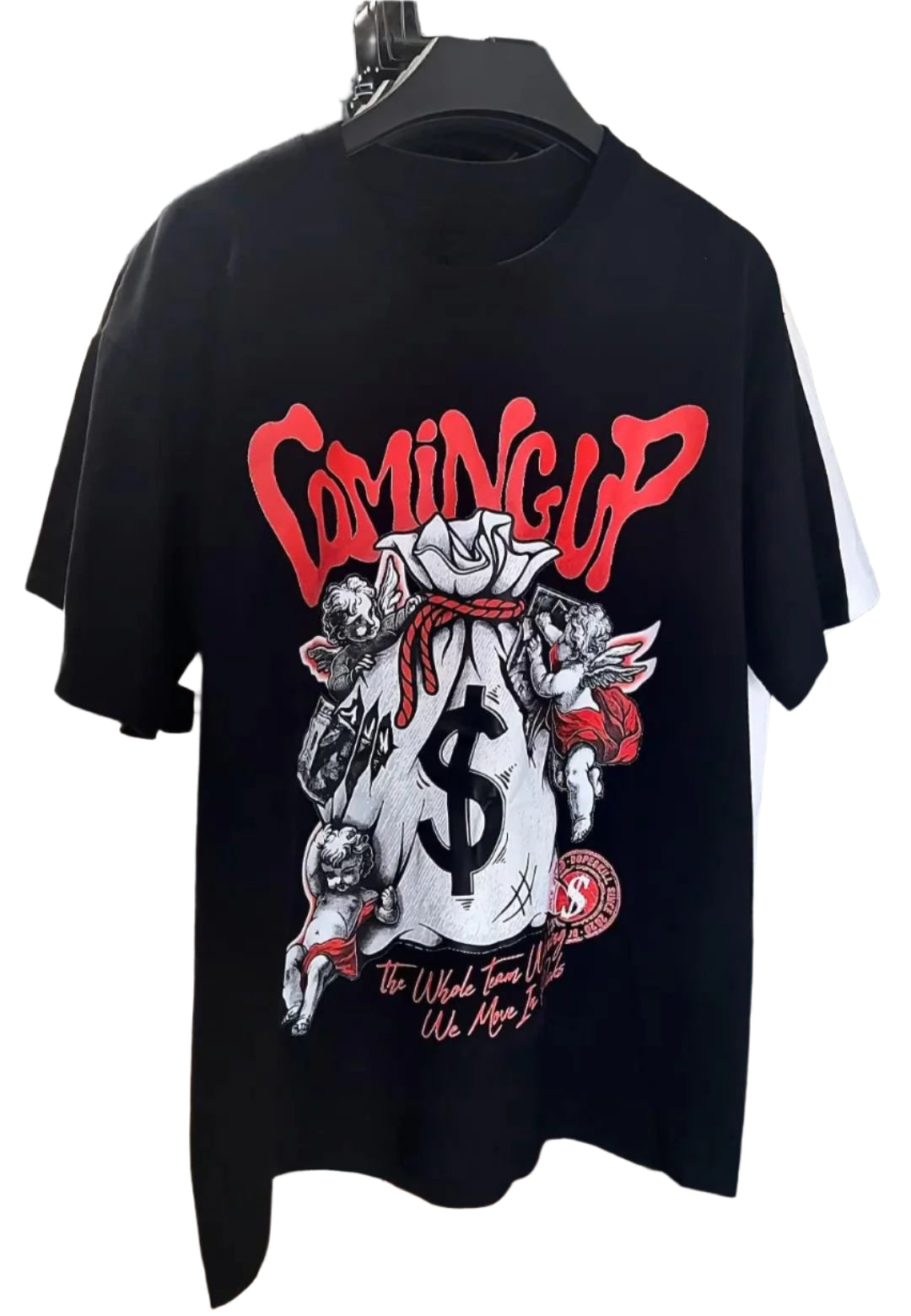 Dark-colored oversize t-shirt with a "Coming Up" text graphic, a money bag with dollar sign, cherub illustrations, and additional text at the bottom.