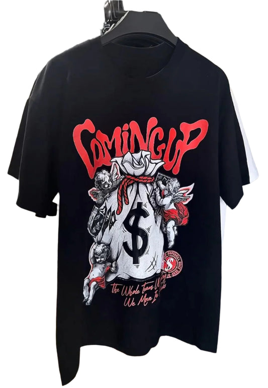 Dark-colored oversize t-shirt with a "Coming Up" text graphic, a money bag with dollar sign, cherub illustrations, and additional text at the bottom.