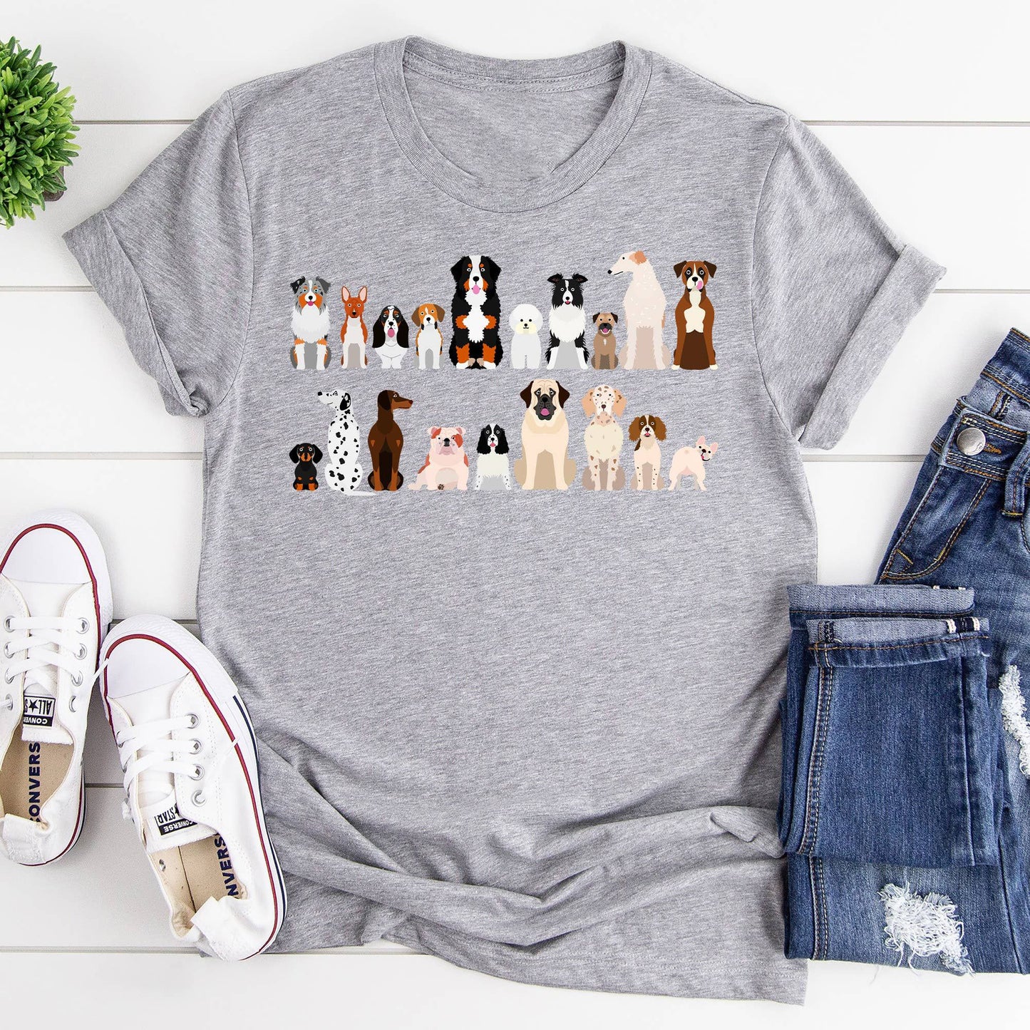  A gray t-shirt with a row of cartoon dog breeds is laid flat with shoes and jeans.