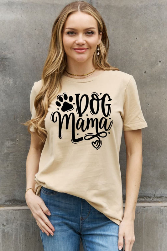 A woman in a beige "Dog Mama" t-shirt with a paw print and heart stands against a textured wall.