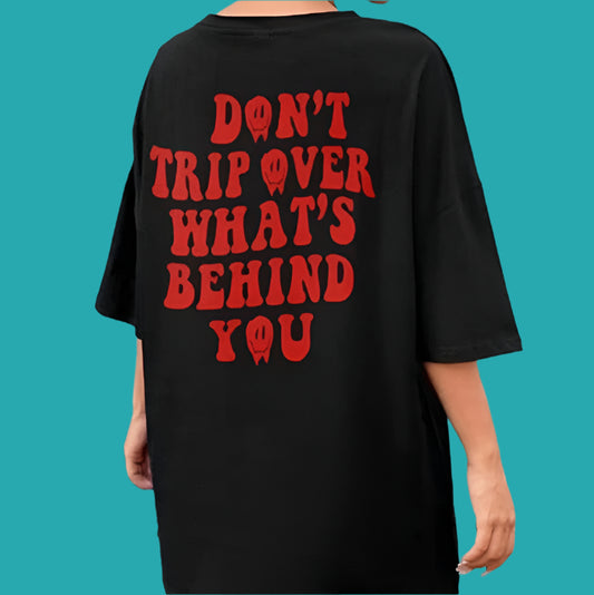 Dark-colored oversize t-shirt with red text that reads "Don't trip over what's behind you" on the back.