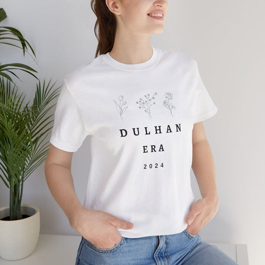 White cotton t-shirt with minimalist floral line art above the text "DULHAN ERA" and "2024" below, suggesting a bride celebrating her wedding year.
