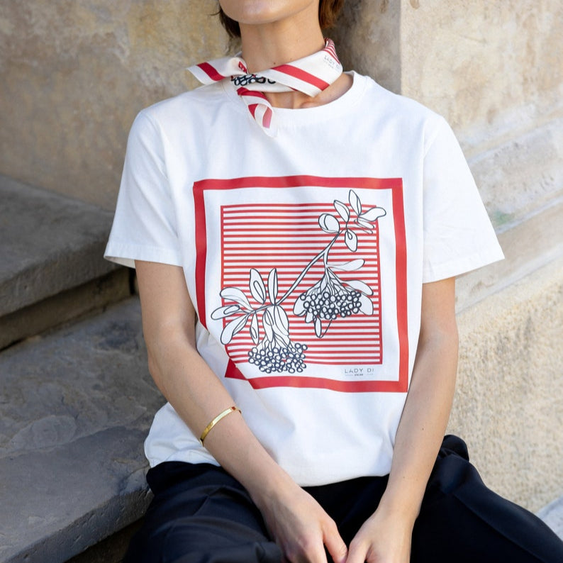 A woman wearing a white t-shirt featuring a red-striped square frame with black and white floral line art.