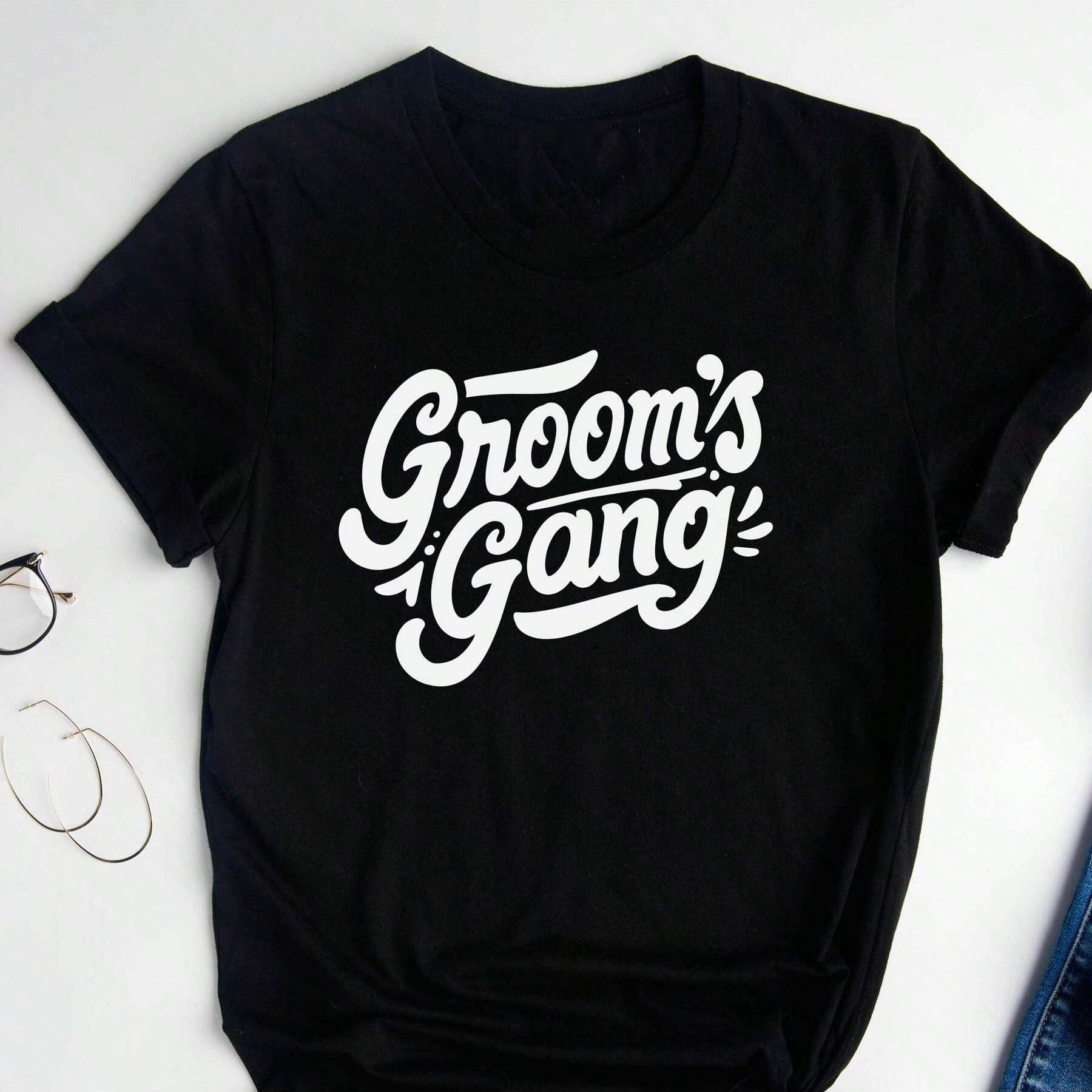 Black cotton t-shirt with white, cursive-style text reading "Groom's Gang".