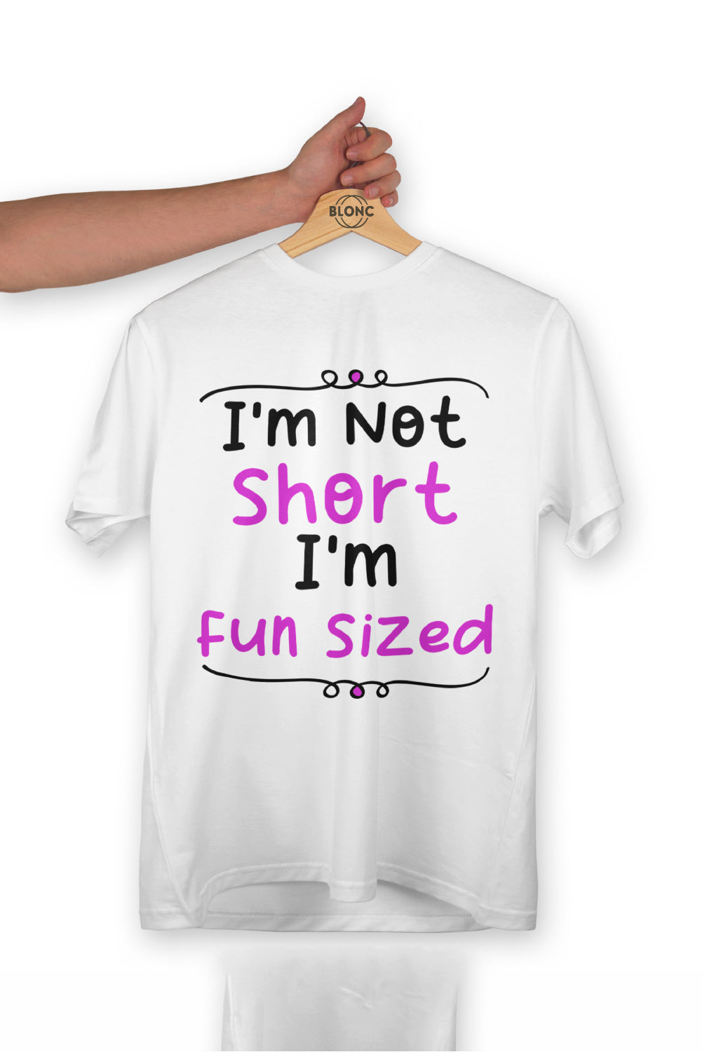 A white t-shirt on a wooden hanger held by an arm, featuring black and pink text "I'm Not Short I'm Fun Sized".