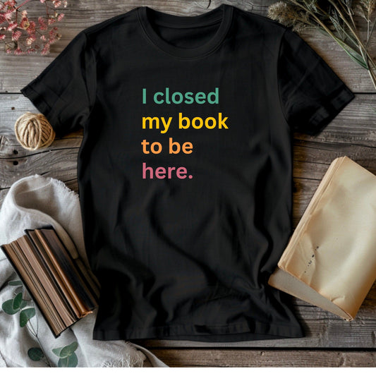 Black t-shirt with "I Closed My Book To Be Here" in colorful lettering.  A humorous statement for book lovers who momentarily pause their reading.
