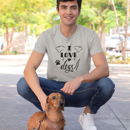A man in a gray "I Love Dogs" t-shirt crouches with a dachshund in a park.