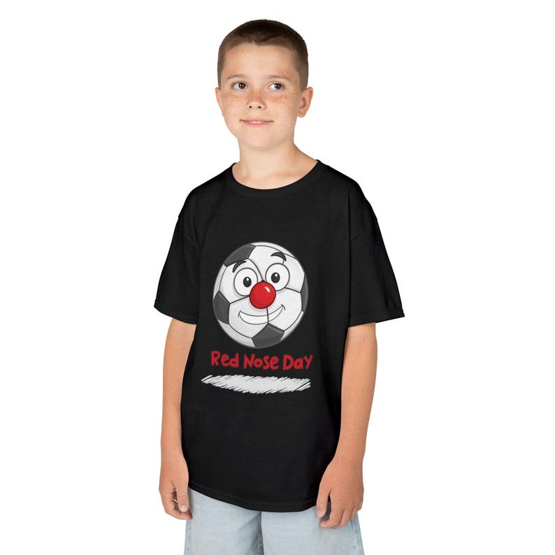 A young boy wears a black t-shirt with a cartoon soccer ball wearing a red nose and the text "Red Nose Day".