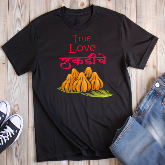Black t-shirt with red text "True Love" above pink Marathi "उकडीचे" and a graphic of orange modaks on a green leaf.