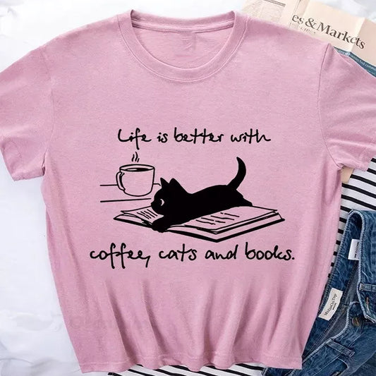 Pink t-shirt with a graphic of a cat on a book, coffee cup, and "Life is better with coffee, cats and books" text.  A cozy design for book lovers.