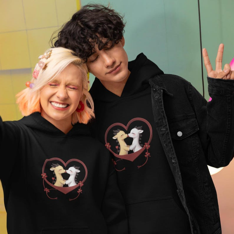 Two people in matching black hoodies with a heart graphic of two cartoon calves kissing.