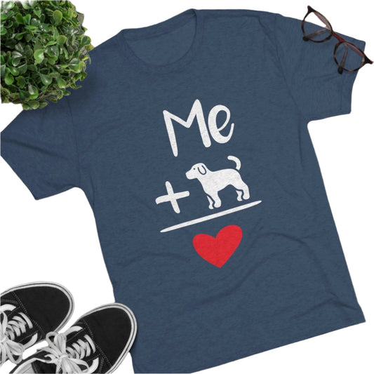 Blue t-shirt with white text "Me + Dog" and a red heart, flat lay on wooden floor with shoes and glasses.