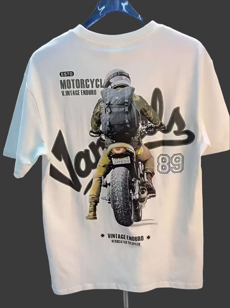 White t-shirt with a graphic of a motorcyclist wearing a backpack, riding a motorcycle from behind, with text "ESTD MOTORCYCL V.INTAGE ENDURO", "Vandals 89", and "VINTAGE ENDURO DEDICATED TO SPEED".