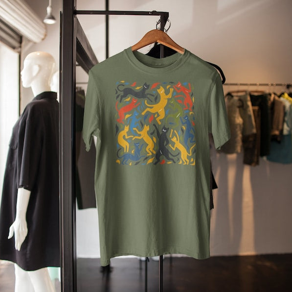 Olive green t-shirt on a hanger features a colorful pattern of dancing cats reminiscent of Matisse's "The Dance."