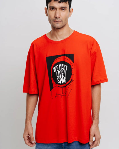  A man with dark hair wears a red t-shirt with a graphic and the text "We Can't Live In Space."