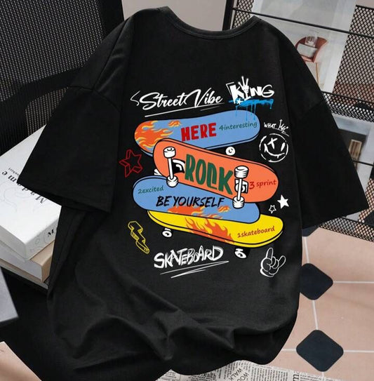 Black oversized t-shirt with a graphic of stacked skateboards, text "Street Vibe King," "HERE," "ROCK," "BE YOURSELF," "SKATEBOARD," and other smaller text and doodle-like illustrations.