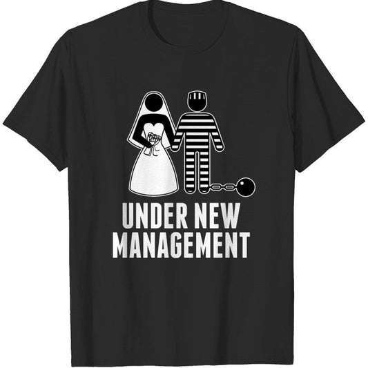 Black cotton t-shirt with a white graphic of a bride holding hands with a groom in prison stripes and a ball and chain, above "UNDER NEW MANAGEMENT" text.
