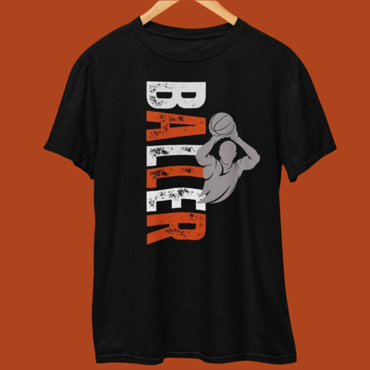 Black T-shirt with a bold vertical 'BALLER' text in distressed white and orange, featuring a gray silhouette of a basketball player shooting a ball, displayed on a hanger.