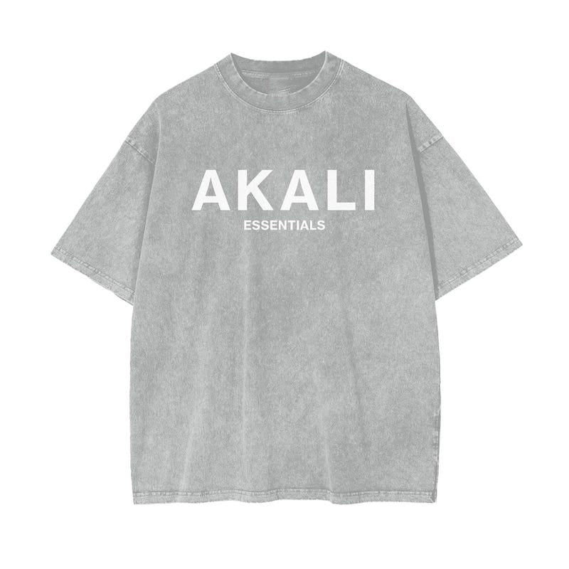 A faded gray t-shirt with "AKALI" and "ESSENTIALS" in white lettering, representing bold faith and a timeless style.