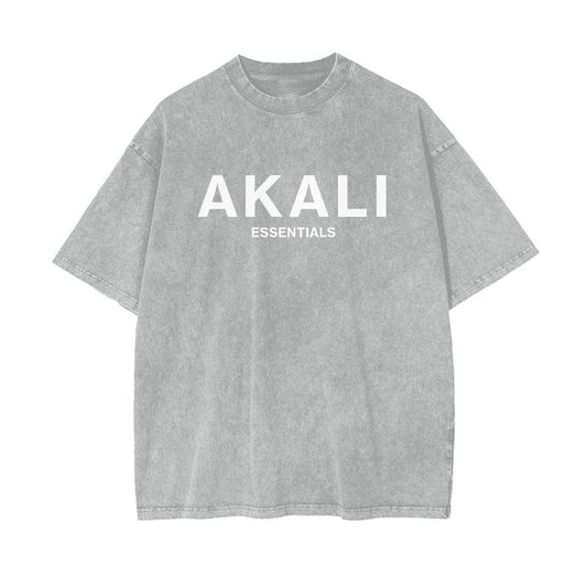 A faded gray t-shirt with "AKALI" and "ESSENTIALS" in white lettering, representing bold faith and a timeless style.