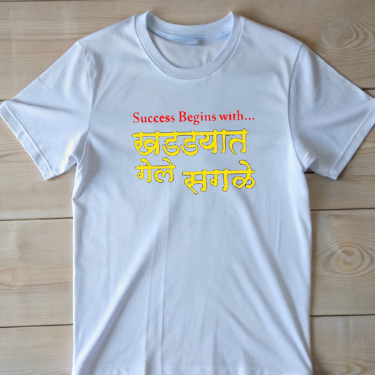 White t-shirt with red English text "Success Begins with..." above yellow Marathi "खड्ड्यात गेले सगळे" (Everything went into the pit).